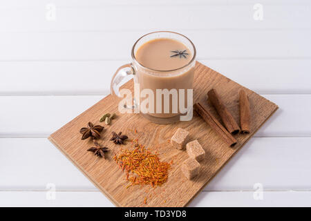 Traditionnel indien Masala chai thé dans une tasse en verre et herbes de cuisine, sur fond de table blanc avec copie espace pour le texte. Banque D'Images