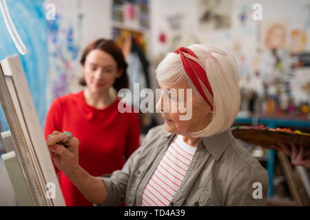 Artiste de dessin. L'artiste aux cheveux gris et de dessin sur toile debout près de curieux étudiant Banque D'Images