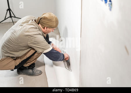 Applique travailleur une feuille de papier peint. Collage homme d'écran sur mur de béton. Remettre en état l'appartement. Concept de rénovation. Peinture papier peint de blanc Banque D'Images