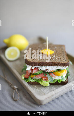 Sandwich avec saumon fumé, poisson rouge, fromage, salade verte, concombre, arugola, poivrons et les graines de sésame sur le pain de seigle dans la plaque de bois. Banque D'Images