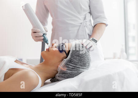 Prenant soin de peau. Très belle femme portant des lunettes spéciales tout en recevant un traitement de la peau du visage Banque D'Images