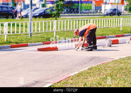 Homme au travail. Peint avec un pinceau la route en béton coloration route limiteur Banque D'Images