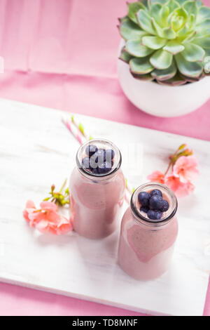 Smoothie fraise banane surmontée de bleuets sur fond rose. Banque D'Images