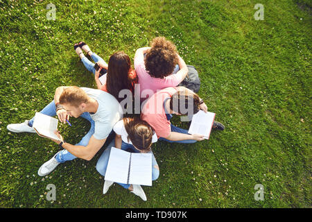 Les élèves étudient assis sur l'herbe verte dans un parc en été au printemps. Les jeunes avec des livres sur la pelouse. Banque D'Images