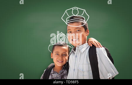 Les jeunes étudiants hispaniques Boy Wearing Backpack avant du tableau noir avec casque de pompier et policier Hat tracé à la craie sur les têtes. Banque D'Images