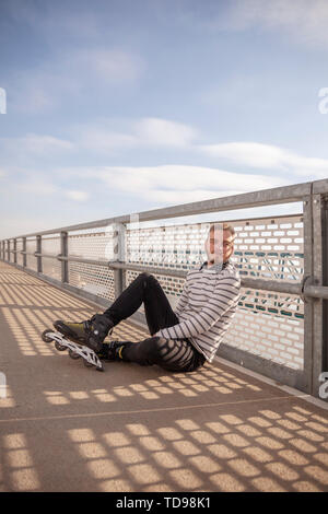 Un jeune homme, posant sur un pont, portant des patins comme activité récréative. Journée ensoleillée à l'extérieur. Banque D'Images