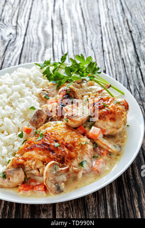 Compotée de poulet avec sauce au vin blanc crème, champignons et légumes et servi avec du riz sur une plaque sur une table en bois foncé - Fricassée de poulet, c Banque D'Images