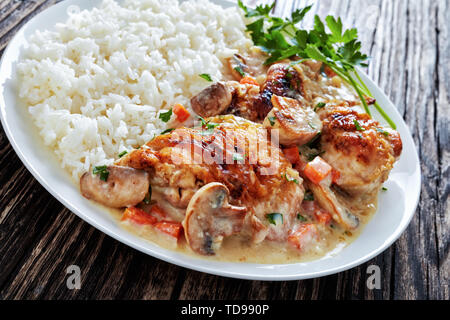 Compotée de poulet avec sauce au vin blanc crème, champignons et légumes et servi avec du riz sur une plaque sur une table en bois foncé - Fricassée de poulet, c Banque D'Images