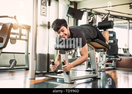 Sport homme asiatique qui s'étend et levage poids par deux jambes lorsque vers le bas pour s'étendant au muscle fitness gym à l'arrière-plan de condominium. Le sport et P Banque D'Images