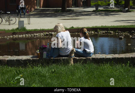 Gdansk Wrzeszcz, Pologne - 2 juin 2019 : Mère et fille s'asseoir en face d'un étang avec un petit chien Banque D'Images