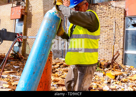 Travailleur senior dans les gants avec casque bleu et gilet de sécurité est la préparation de l'équipement de soudage à gaz pour couper la ferraille, les bouteilles à GPL et Nitro Banque D'Images