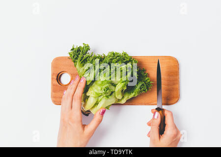 Overhead View woman's hands holding salade coupe couteau et tête de laitue verte sur planche en bois sur le tableau blanc. Banque D'Images