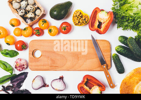 Vue de dessus du vide planche à découper en bois avec couteau entre les légumes frais, œufs de caille, de noix et de pain croustillant sur fond blanc, télévision lay. Banque D'Images