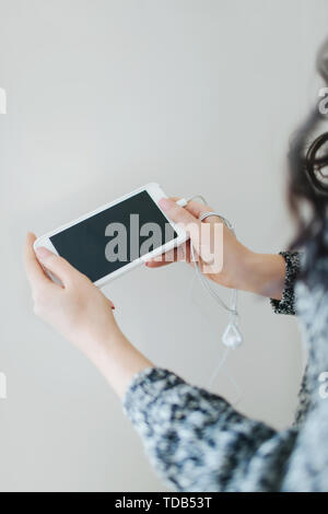 Young woman holding white smartphone avec le casque sur un fond blanc. Banque D'Images