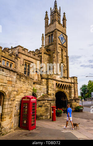 Un homme qui marche un chien passé Eastgate et St Peter's Chapel à Warwick, Warwickshire, Royaume-Uni. L'été 2018. Banque D'Images