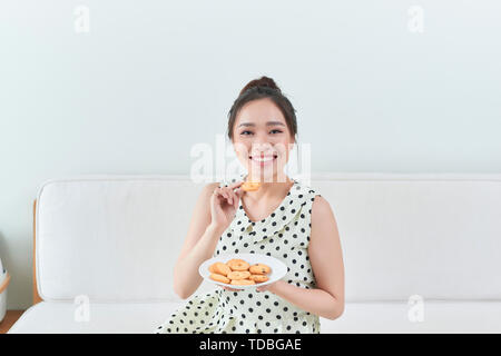 Happy girl eating a cookie diététiques assise sur un sofa à la maison Banque D'Images