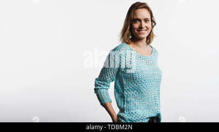 Happy woman wearing a woollen haut standing against white background. Femme souriante avec les cheveux bruns courts looking at camera. Banque D'Images