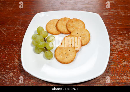 Craquelins au fromage rond avec des raisins sur une place blanche Banque D'Images