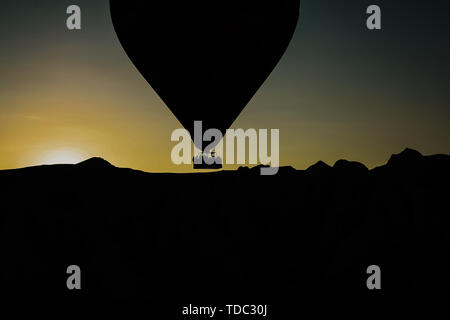 Silhouette d'affaires et des touristes voler au-dessus de la montagne au coucher du soleil dans un ballon aérostatique. Banque D'Images