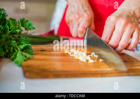 La main de femme avec un couteau tranches d'ail sur la planche à découper en bois dans la cuisine. Selective focus Banque D'Images