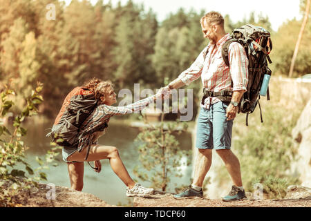 Homme agréable joyeuse aidant son amie à monter Banque D'Images