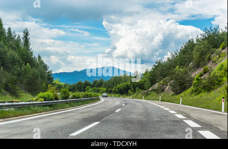 Autoroute ou route dans les montagnes avec un marquage clair entouré d'arbres verts vibrant sous ciel bleu. Vue imprenable sur la montagne et dans l'arrière-plan Banque D'Images
