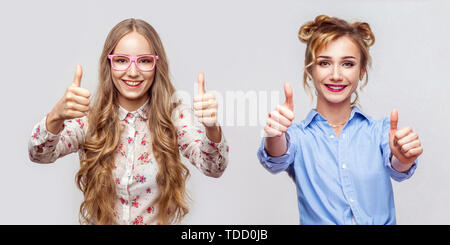 Portrait de deux heureux belle blonde jeune femme de style casual avec le maquillage et la coiffure, permanent Thumbs up, looking at camera avec sourire à pleines dents. Banque D'Images