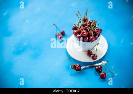 La composition créative de cerise mûre fraîche dans une tasse wite avec copie espace isolé sur fond bleu un style minimaliste. Concept d'été amusant et sain Banque D'Images