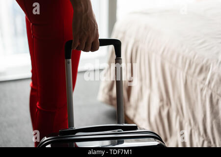 Close-up la main tenant la poignée valise. Businesswoman arrive dans une chambre d'hôtel avec valise noire. Femme en costume d'affaires de corail rouge. Banque D'Images