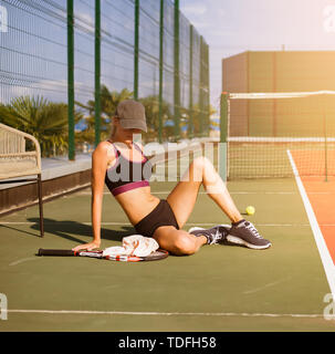 Jeune fille Slim tennis athlète joueur est sur l'open de tennis en été. Siège sur le plancher Banque D'Images