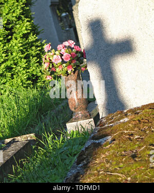 Ombre de croix sur la tombe, tombe avec des fleurs artificielles Banque D'Images