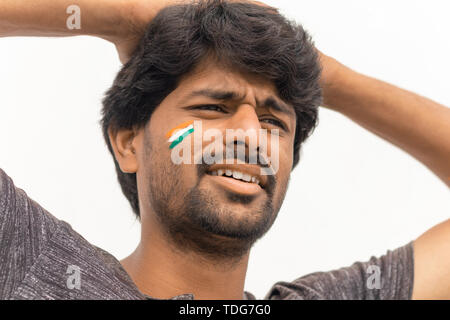 Closeup Shot, expression triste de Cricket Indien avec fan de sport drapeau indien peint sur le visage, l'arrière-plan isolé Banque D'Images