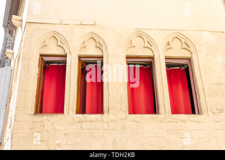 Montpellier, France. Quatre fenêtres avec des rideaux rouges et des décorations dans la vieille ville Banque D'Images