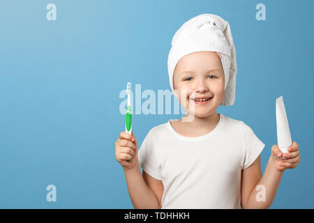 Closeup portrait d'une petite fille sur un fond bleu. Un enfant avec une serviette blanche sur la tête tenant une brosse à dents et dentifrice. Le concept de dai Banque D'Images