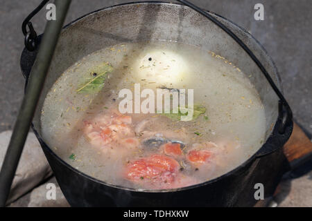 Le saumon rouge délicieux poissons frais cuits dans la soupe de grand joueur sur feu de l'extérieur. La cuisson des aliments sur le feu pendant le pique-nique journée ensoleillée. Banque D'Images