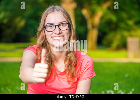 Une jeune femme tient son pouce vers le haut et de sourires Banque D'Images