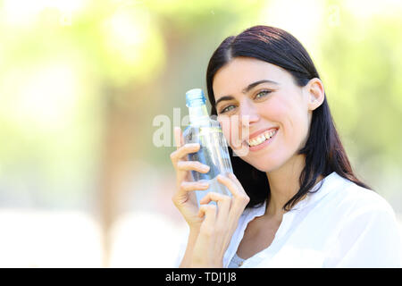 Heureux femme tenant une bouteille d'eau en vous regardant debout dans un parc avec un fond vert Banque D'Images