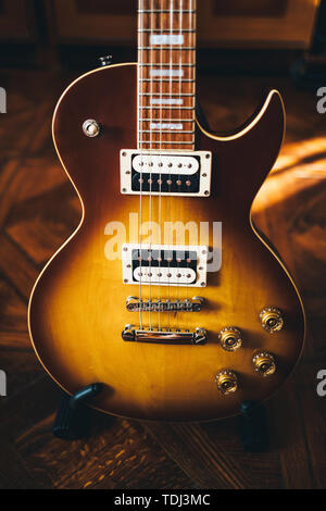 Guitare électrique avec brown sunburst corps debout sur le stand dans la salle ensoleillée avec plancher en bois. Banque D'Images