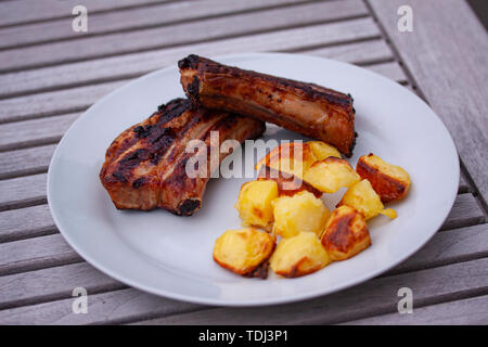 Sticky barbecue côtes et côtelettes de porc au four avec grill de pommes de terre au four sur une plaque avec fond de bois. Banque D'Images