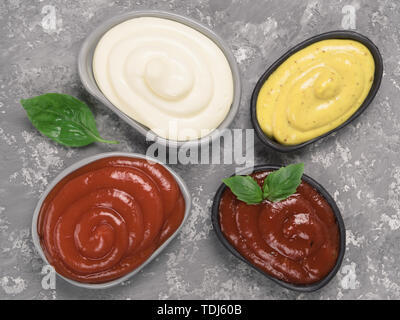 Vue du dessus de l'ensemble des sauces classiques dans le quartier branché de plaques sur fond de béton gris. Set - salsa Sauces, moutarde, ketchup, mayonnaise et Vinaigrette basilic pour. Mise à plat. Banque D'Images