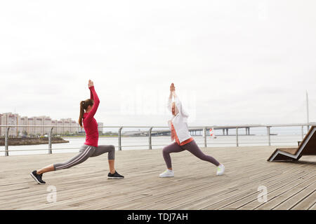 Vue de côté portrait de deux femmes faisant du yoga sur la jetée de matin, copy space Banque D'Images