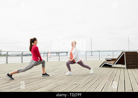 Vue de côté portrait de deux jeunes femmes qui s'étend les jambes tout en faisant du yoga sur la jetée en bois, copy space Banque D'Images