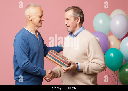 Beau contenu mature man in sweater holding dépouillé boîte cadeau et main tremblante de l'ami(e) tout en acceptant des voeux d'anniversaire at party Banque D'Images