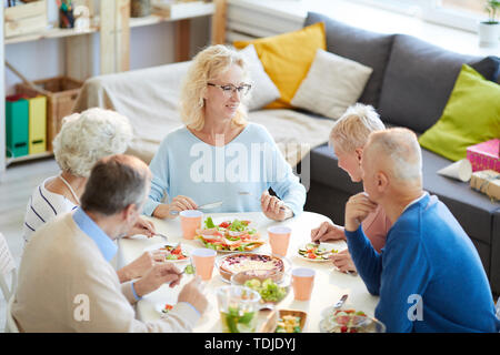 Happy attractive young woman with blonde cheveux bouclés assis à table et de dîner avec des amis Banque D'Images