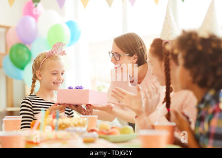 Portrait of cute little girl recevoir cadeau de maman au cours d'anniversaire avec des amis, copy space Banque D'Images