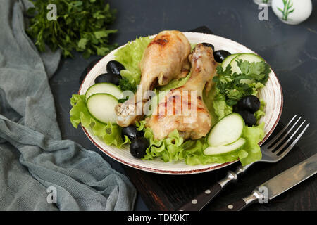 Pilons de poulet servi avec des concombres, des olives noires et la laitue dans une assiette sur un fond sombre, photo horizontale Banque D'Images