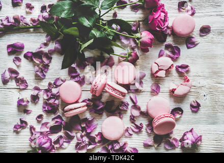 Macaron rose sucré cookies et au printemps, les bourgeons de fleurs de rose et les pétales sur fond de table en bois, vue du dessus. La texture des aliments, l'arrière-plan et de papier peint Banque D'Images