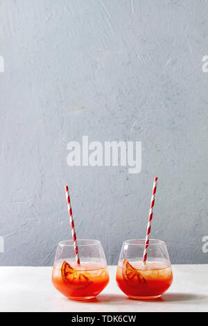 Orange sanguine cocktails glacés dans les verres, décorés par tranche de l'orange, servi avec de la paille rétro sur table en marbre blanc avec mur gris à l'arrière-plan. Banque D'Images