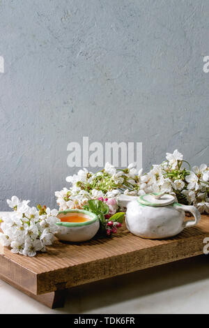 Fait main artisanat théière et tasse en céramique avec du thé chaud décoré par des branches de cerisier en fleurs au printemps sur le plateau de service en bois de style japonais sur blanc en t Banque D'Images