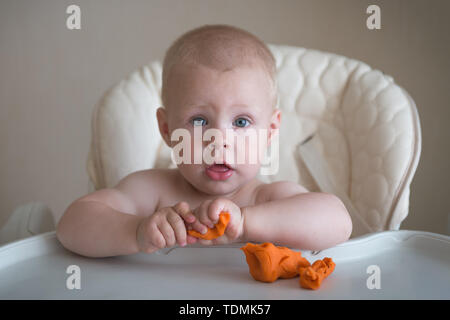 La créativité des enfants. Le bébé tente de sculpter de l'orange de l'argile. Cute little boy moule à partir de la pâte à modeler sur la table. Banque D'Images